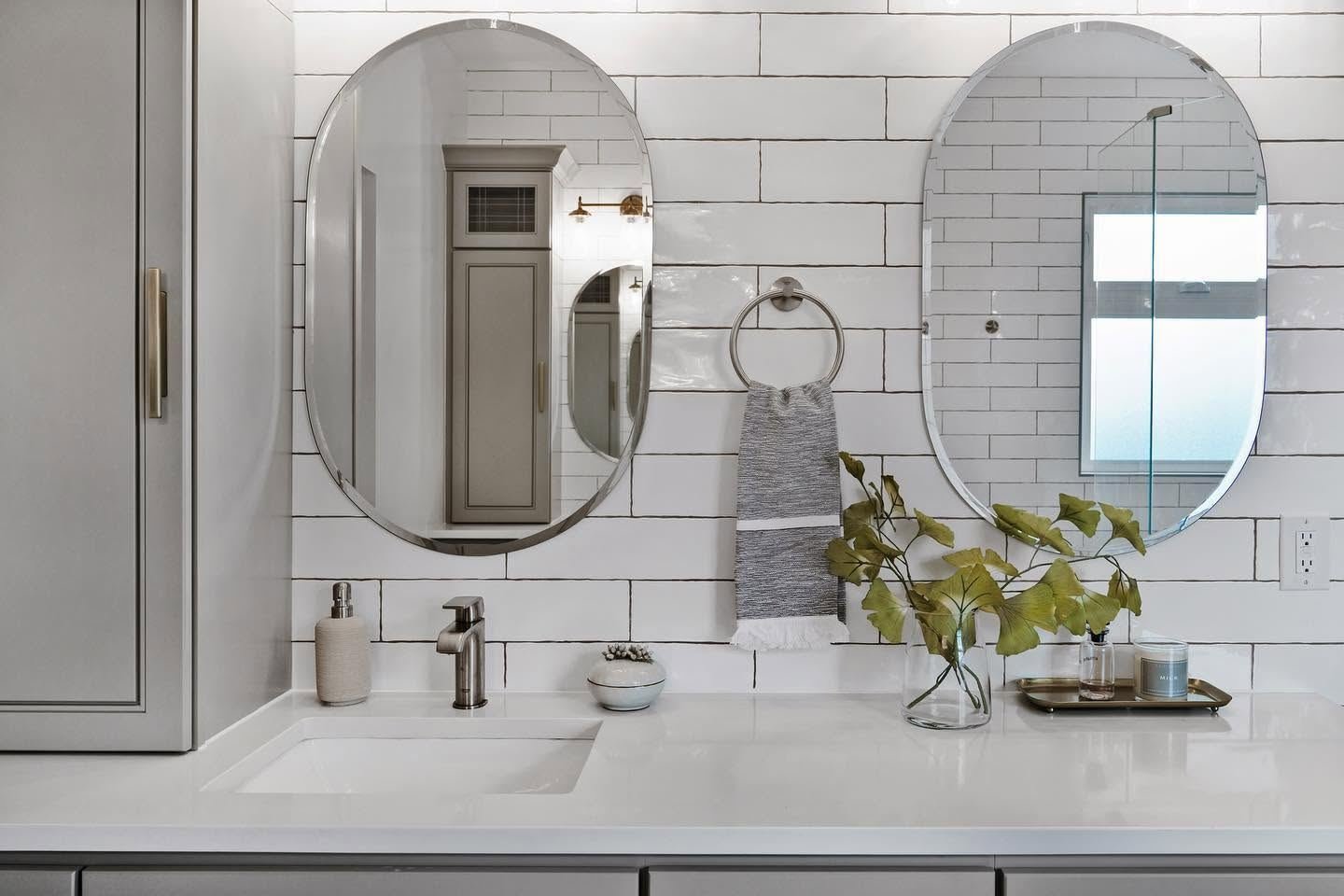 Twin oval mirrors over a white quartz vanity with handmade-look white tile