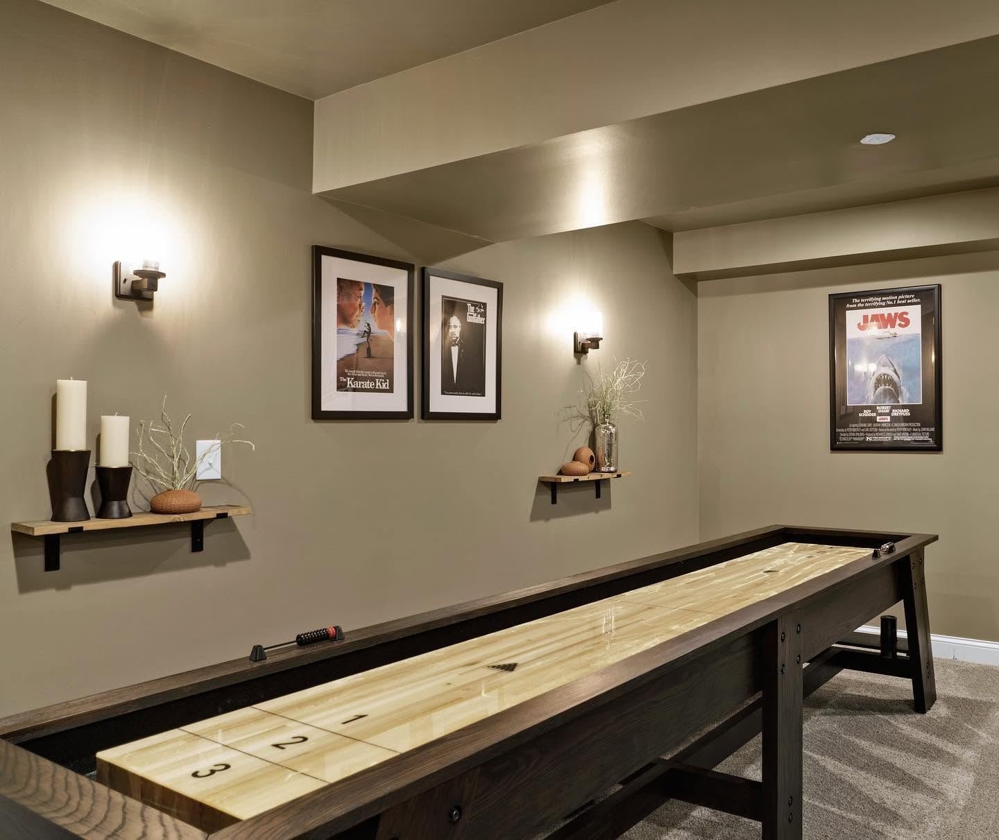 Lower-level game room with a shuffleboard table, sconces and framed posters
